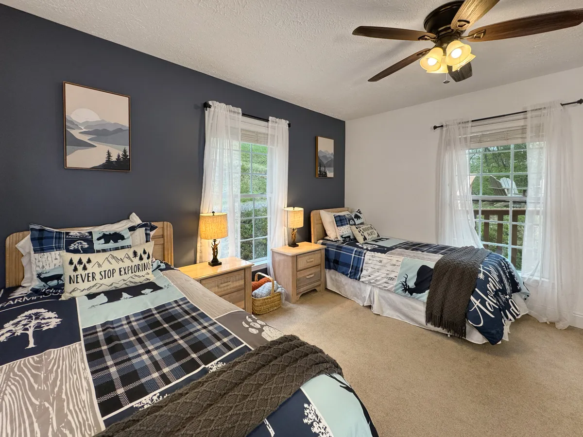 A cheerful bedroom featuring two beds with distinct, colorful bedding, large windows flooding the space with natural light, and decorative wall art. The room is bright, relaxed, and ideal for families or friends traveling together.