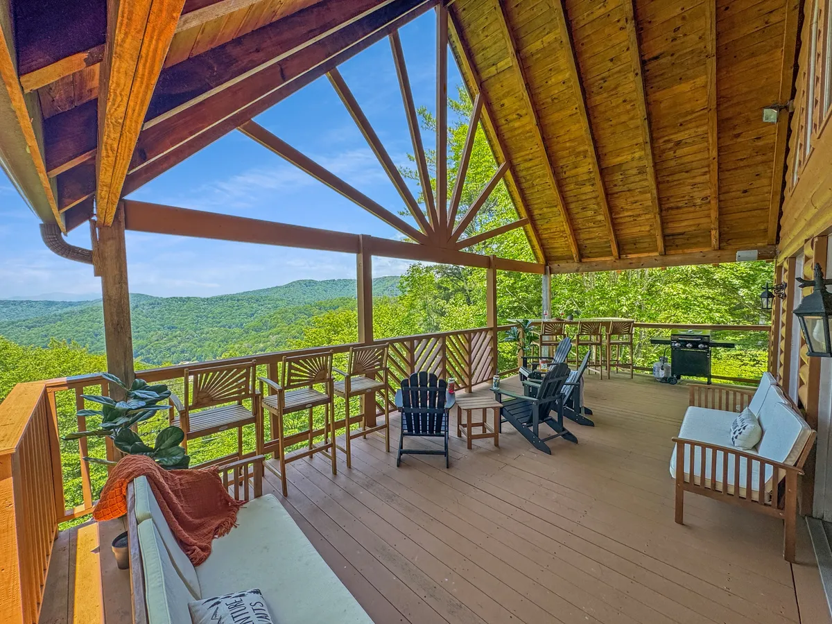 A spacious wooden deck with comfortable seating and an outdoor grill overlooks a sweeping mountain view. The scene suggests relaxation and socializing, offering a taste of resort-style outdoor living and the surrounding natural beauty.