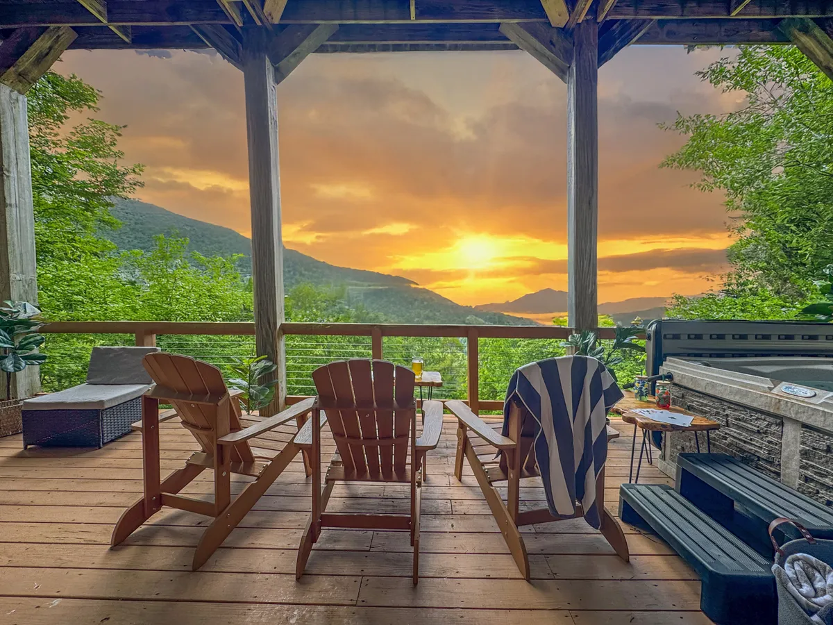 A serene wooden deck with comfortable chairs and a hot tub overlooking a beautiful mountain landscape at sunset. The scene exudes relaxation and offers a sense of privacy, perfect for unwinding after a day of activities.