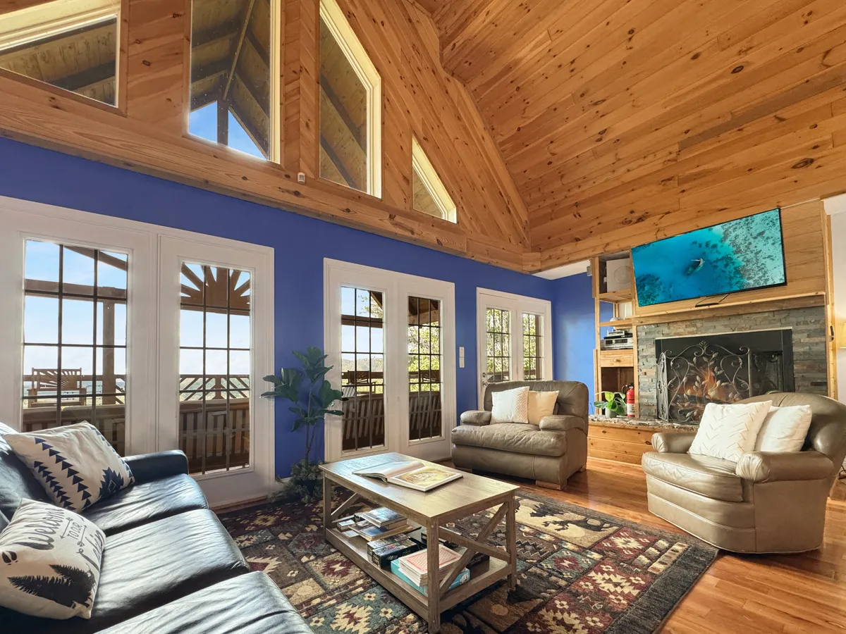 A comfortable living area with expansive windows, a wooden ceiling, and soft, inviting seating arranged around a coffee table. The room offers mountain views, a warm atmosphere, and elements that encourage family relaxation, conversation, and enjoyment of the natural scenery.