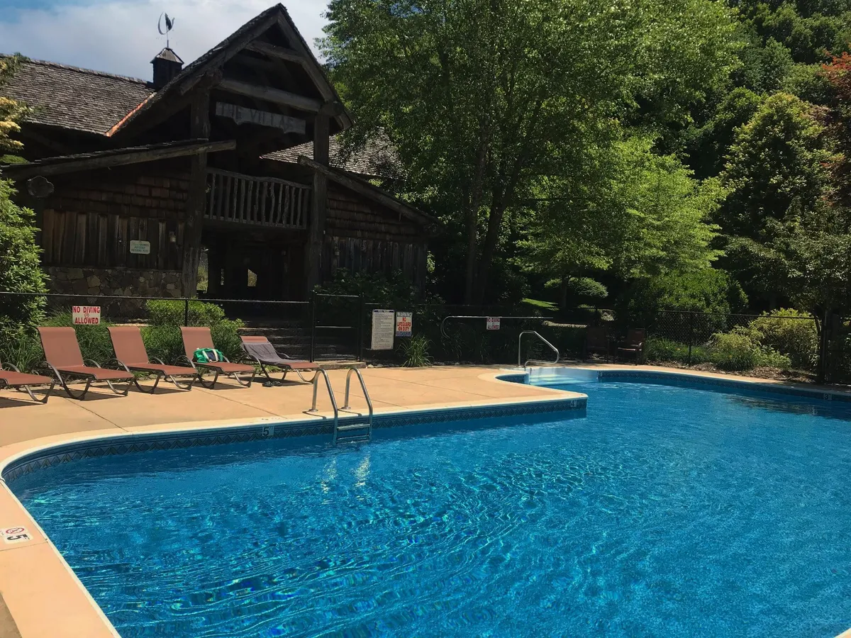 A sparkling swimming pool surrounded by lounge chairs, with a cabin-like building and lush greenery in the background. The area looks inviting for relaxation, play, and socializing, suggesting a vibrant, family-friendly atmosphere.